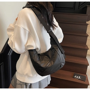 Detailed view of black nylon crescent bag worn crossbody against a wooden staircase