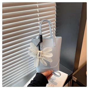 Close-up of light blue mini tote bag featuring a 3D white flower charm and matte leather finish