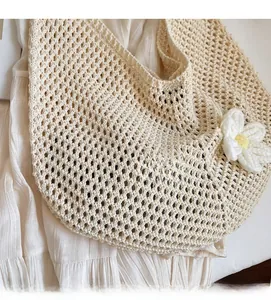 Close-up of cream knit tote bag showing hollow-out mesh weave and a large floral charm