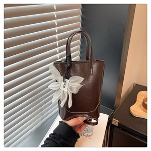Detail of dark brown leather tote bag with elegant white floral charm and fine stitching