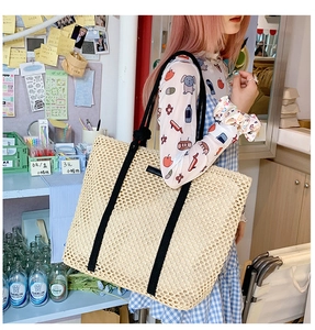 Detailed close-up of beige woven tote bag with contrasting black thick rope handles