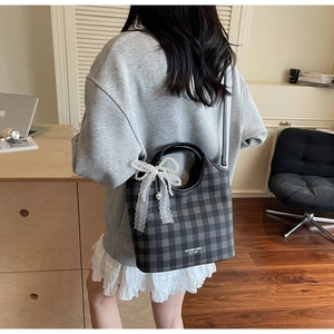 Détail d'un sac à carreaux avec un nœud en dentelle et un pendentif perle élégant