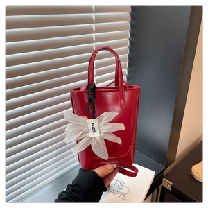 Detail of red glossy leather bucket bag with organza flower charm and logo lettering