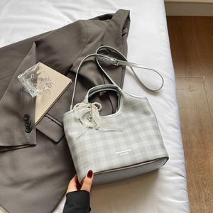 Détail d'un sac à carreaux argenté orné d'un nœud en dentelle perlée sur lit blanc
