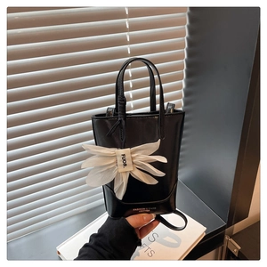 Close-up of black leather bucket bag with white floral charm and adjustable shoulder strap