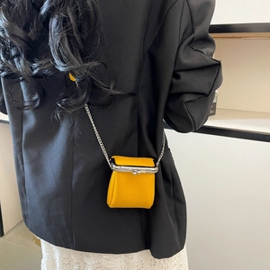 Detail of a bright yellow mini kiss-lock bag with lychee texture and silver chain strap