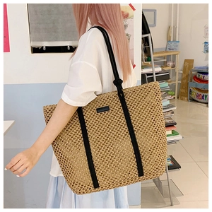 Detail of hollow mesh woven straw tote bag with black straps and minimalist label