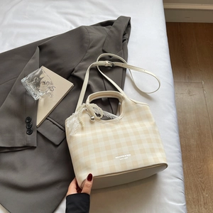 Détail du sac cabas beige à carreaux avec bordure en dentelle et pendentif en perles