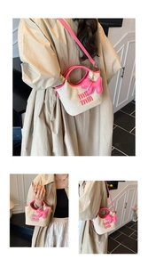 Detail of woven straw tote bag featuring pink leather handles and letter logo decoration