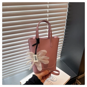 Pink synthetic leather tote bag detail with white flower charm and long shoulder strap