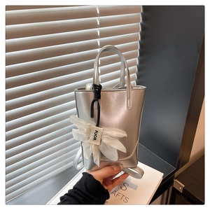 Close-up of silver metallic mini bucket bag with white mesh bow charm and logo detail