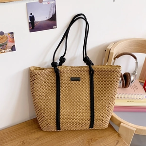 Close-up of woven straw tote bag with black rope handles on a wooden table setup