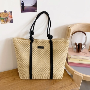 Detail of beige straw tote bag with honeycomb weave and black rope handles on wood table