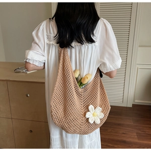 Close-up of a hollow knit shoulder bag featuring a white daisy crochet charm and floral accents