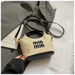 Detail of handwoven straw bucket bag with black leather handle and embroidered logo