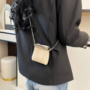 Crossbody view of a mini cream leather lipstick bag with silver chain and clip clasp