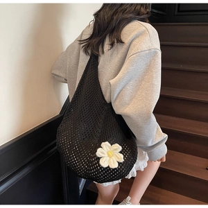 Detail of black mesh tote bag with large white daisy crochet flower on wooden background