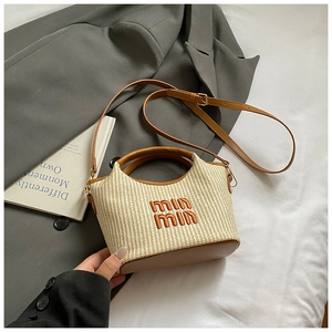 Detail of woven straw handbag featuring brown leather handles and embroidered logo