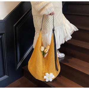 Detail of yellow knit tote bag featuring a white floral ornament and black leather strap