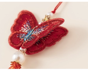 Detailed macro view of red butterfly embroidery with golden threads and orange tassels