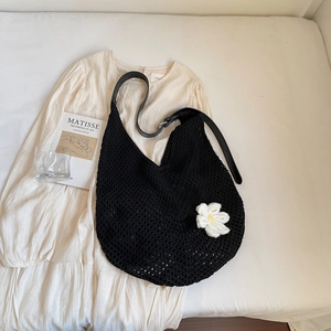 Detail of black crochet shoulder bag with white daisy charm on a white dress