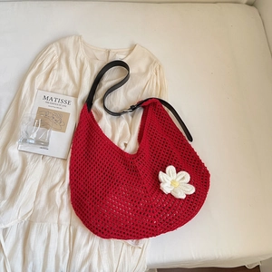 Close-up of red crochet shoulder bag featuring white daisy decor and black leather strap
