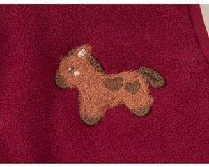 Détail rapproché du tissu polaire rouge foncé avec un écusson brodé de poney marron