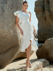 Detail of elegant white one-shoulder dress with ruffle trim and side slit on beach rocks