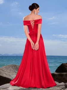 Elegante abito da sera rosso in raso con spalle scoperte e schiena intrecciata in spiaggia