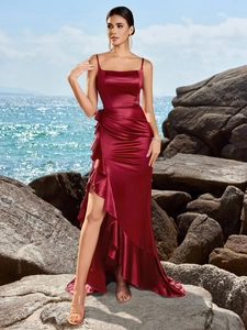 Elegant wine red satin evening gown with thin straps and ruffled high slit hem in a seaside setting