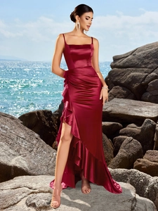 Elegant wine red satin evening gown with ruffles and a side slit on a scenic beach