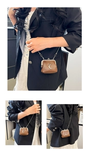 Detail of a brown leather mini crossbody bag with silver moon decor and ball chain