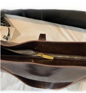 Detailed close-up of smooth gold zipper hardware on a dark brown leather tote bag