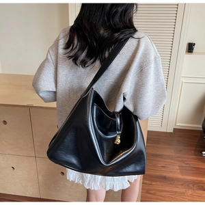 Detail of black glossy leather tote bag with gold charm on shoulder in cozy setting