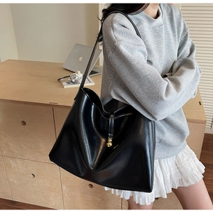 Close-up of black leather tote bag with gold ball clasp shown on a model for daily commute