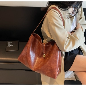 Detail of dark brown leather tote bag with gold charm worn by a model in a trench coat