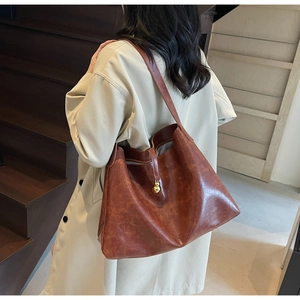 Detailed close-up of a brown leather tote bag with a golden metal bead accent and rich texture