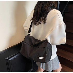 Vue arrière du modèle portant un grand sac bandoulière en nylon noir avec logo BNT