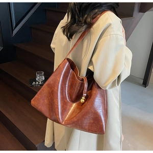 Brown faux leather tote bag with gold ball charm shown on a beige trench coat