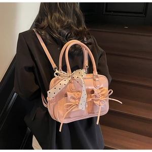 Dettaglio dello zaino in pelle rosa con fiocchi decorativi e foulard a pois sul manico
