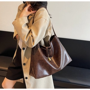 Detail of deep brown leather tote bag with unique golden gourd-shaped charm