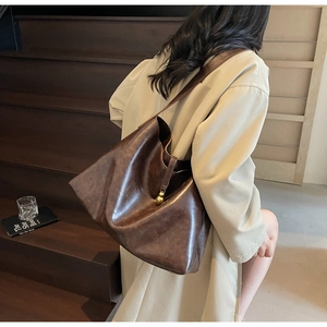 Close-up of vintage brown leather tote bag with a decorative gold ball charm pendant