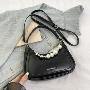 Close-up of black crescent shoulder bag with pearl heart chain on denim background