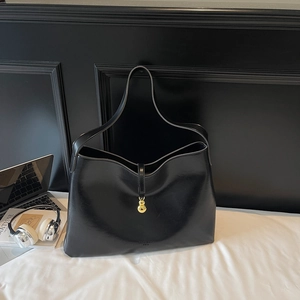 Macro shot of glossy black tote bag with gold gourd pendant and minimalist accessories