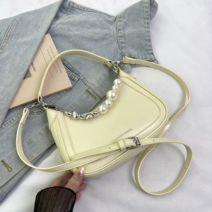 Detail view of cream saddle shoulder bag with pearl and heart-shaped metal chains