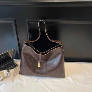 Detail view of large dark brown leather tote bag with elegant golden gourd pendant charm