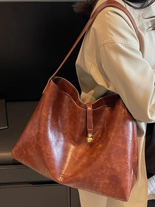 Brown vintage faux leather tote bag with gold ball charm on a model in trench coat