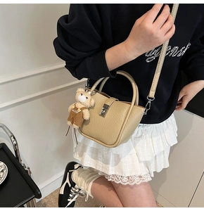 Détail du sac seau beige à motif litchi avec breloque ours et boucle métallique