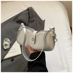 Detail of silver metallic baguette bag with turn-lock closure on white bedding background