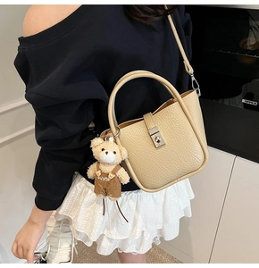 Détail du sac seau beige en cuir avec fermoir rotatif argenté et charmant pendentif ours
